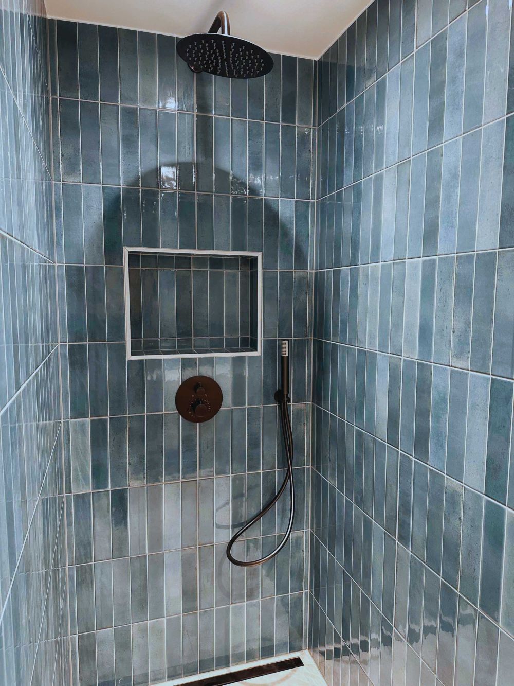 Douche à l’italienne avec faïence murale bleue verticale, niche intégrée et robinetterie noire – Pose et aménagement AK dans le Pays de Gex