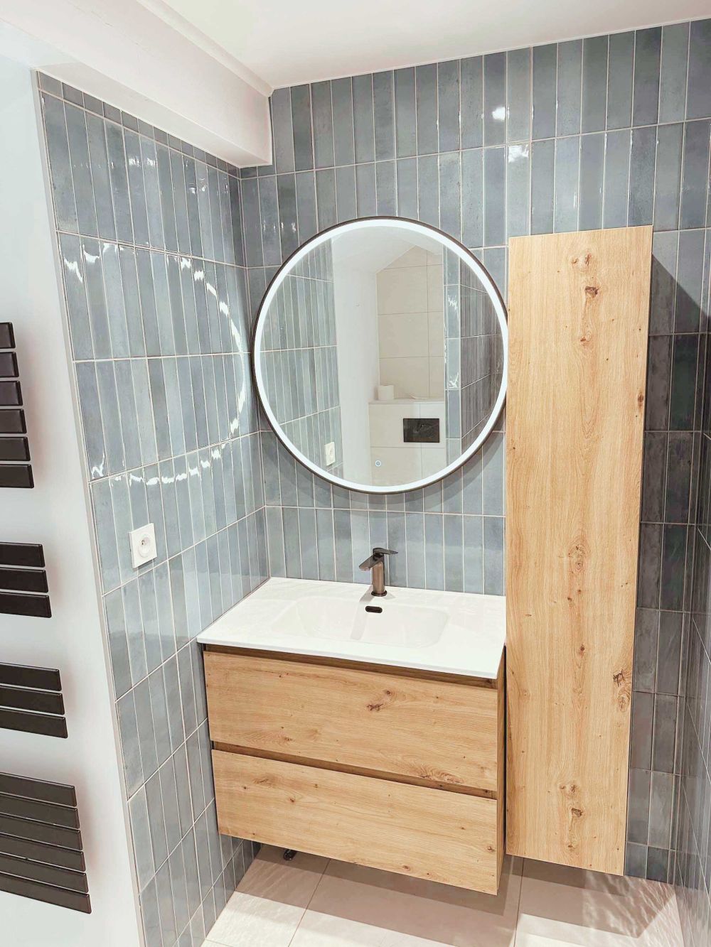 alle de bain moderne avec carrelage mural bleu vertical, meuble suspendu en bois et miroir LED circulaire – Rénovation AK dans le Pays de Gex